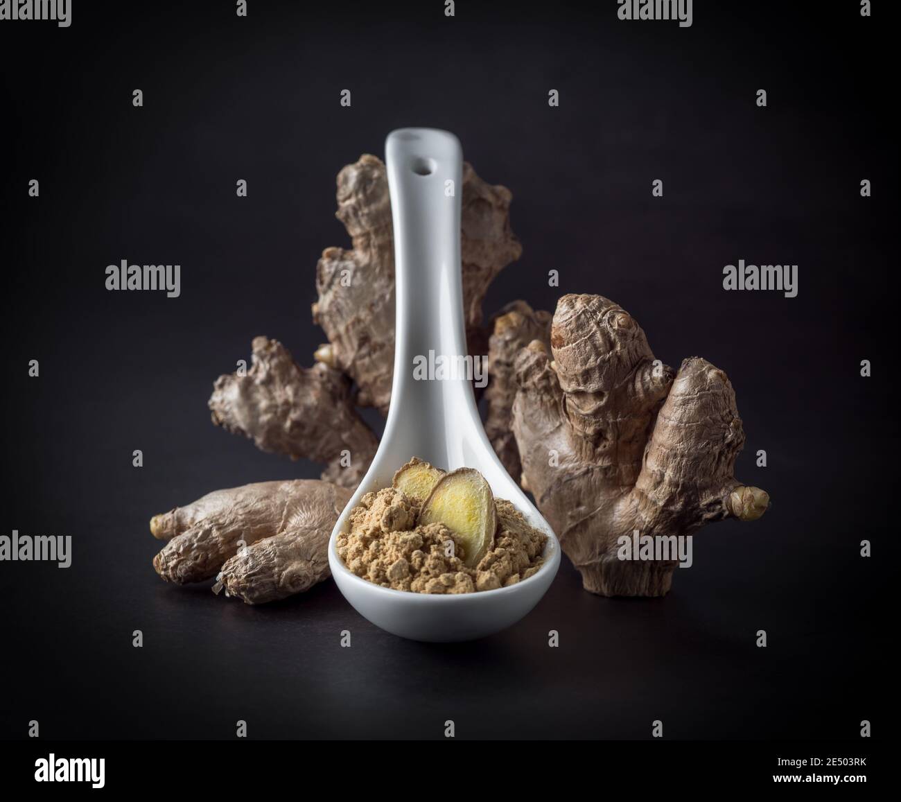 Radice di zenzero e polvere di zenzero in un cucchiaio isolato su sfondo nero, primo piano. Foto Stock