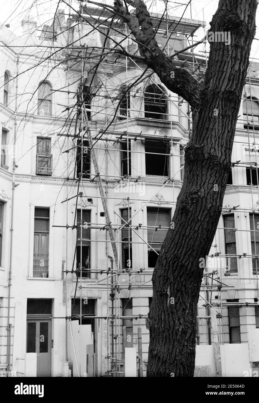 UK, West London, Notting Hill, 1973. Rundown e faticosamente grandi case a quattro piani stanno iniziando ad essere restaurate e ridecorate. Di fronte a circa 20 Powis Square dall'area giochi di Powis Square. Impalcature è in uso su una casa. Foto Stock