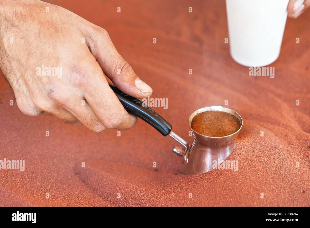 Il caffè preparato sulla strada in modo arabo tradizionale, cezve o ibrik (piccola caffettiera turca) viene posto in sabbia rossa calda fino a che il liquido non bolle Foto Stock