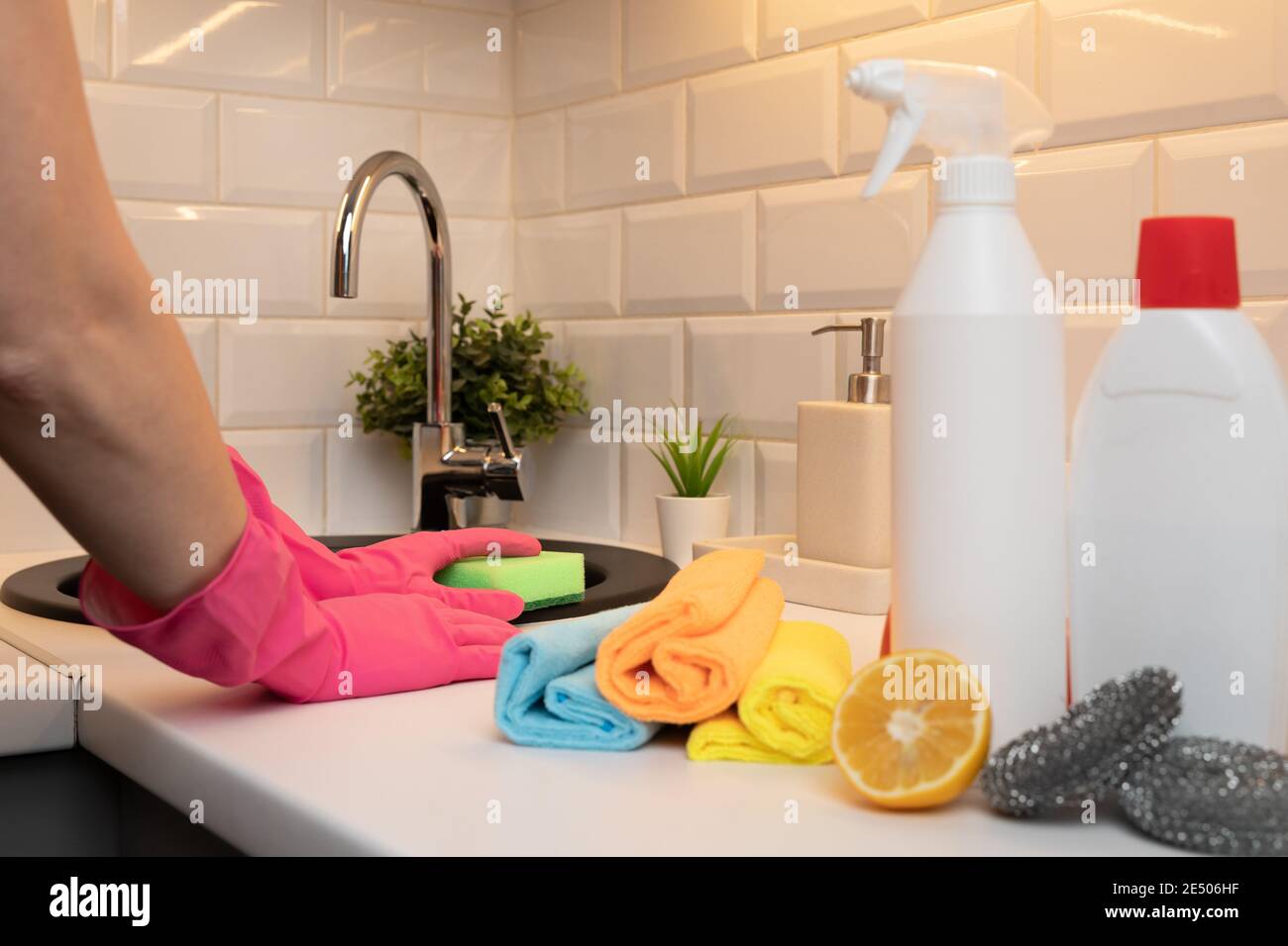 Donne pulizia lavello cucina con guanti e spugna e davanti prodotti di pulizia sfocati per la disinfezione. Foto Stock