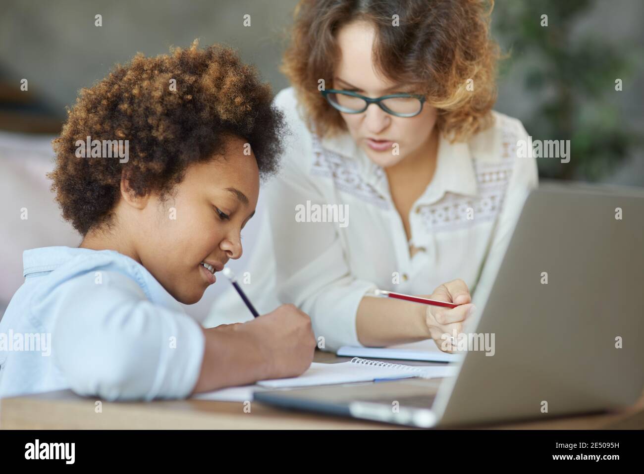 Impegno per l'eccellenza. Entusiasta razza mista teen studentessa scrivere durante una lezione con la sua insegnante femminile a casa Foto Stock