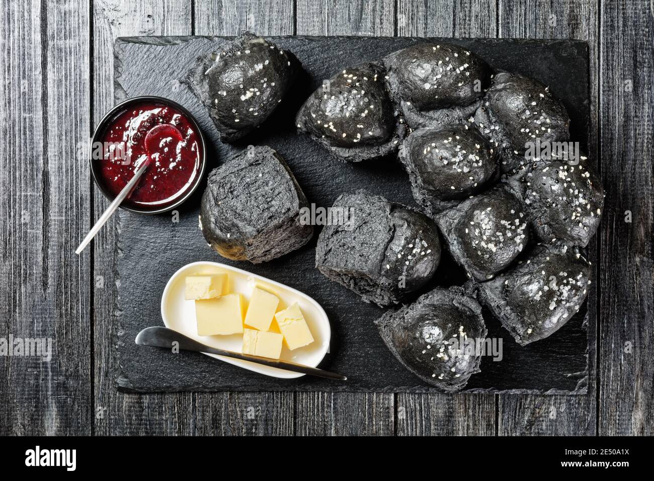 Ciambelle nere cosparse di sale marino sulla parte superiore in impasto di lievito al carbone attivo servito su una tavola di ardesia nera su un tavolo di legno nero con cubetti di b Foto Stock