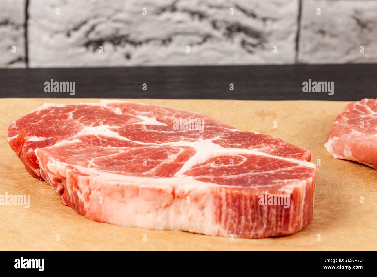 bistecca di carne di maiale cruda su carta pergamena marrone su tavolo nero contro sfondo grigio muro mattone Foto Stock