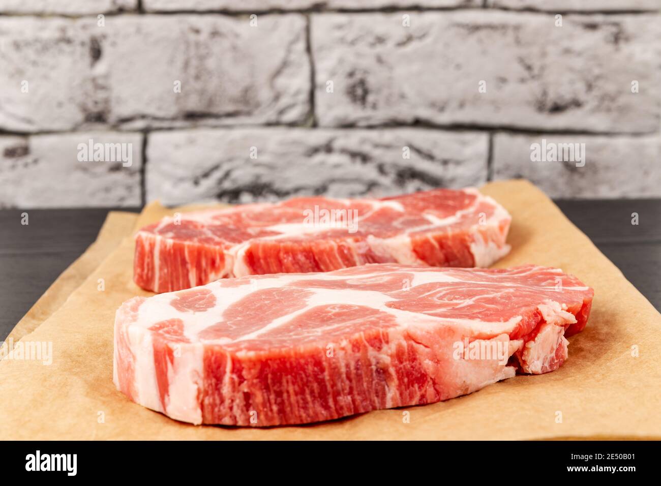 bistecca di carne di maiale cruda su carta pergamena marrone su tavolo nero contro sfondo grigio muro mattone Foto Stock