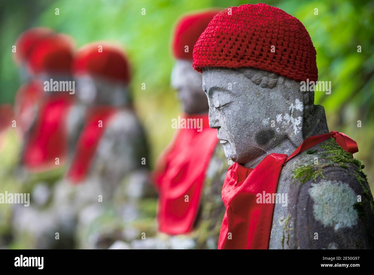Primo piano di una fila di statue jizo giapponesi in pietra che indossano bibs rossi e berretti, contro uno sfondo bokeh Foto Stock