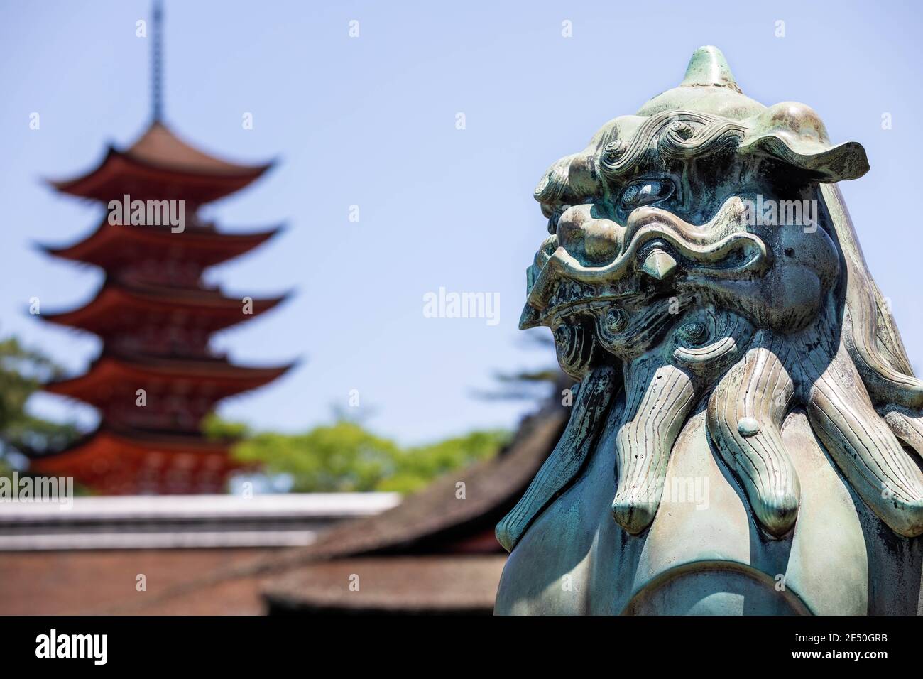 Primo piano di una statua di bronzo di un leone giapponese, con un pagod rosso sullo sfondo Foto Stock