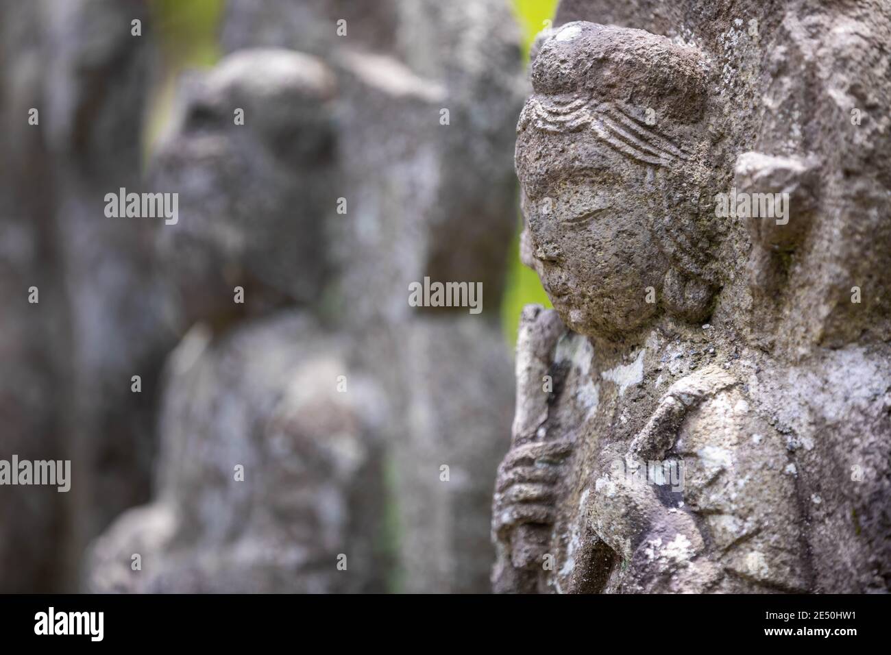 Primo piano di una fila di antiche statue giapponesi in pietra e bassorilievi, su uno sfondo bokeh Foto Stock