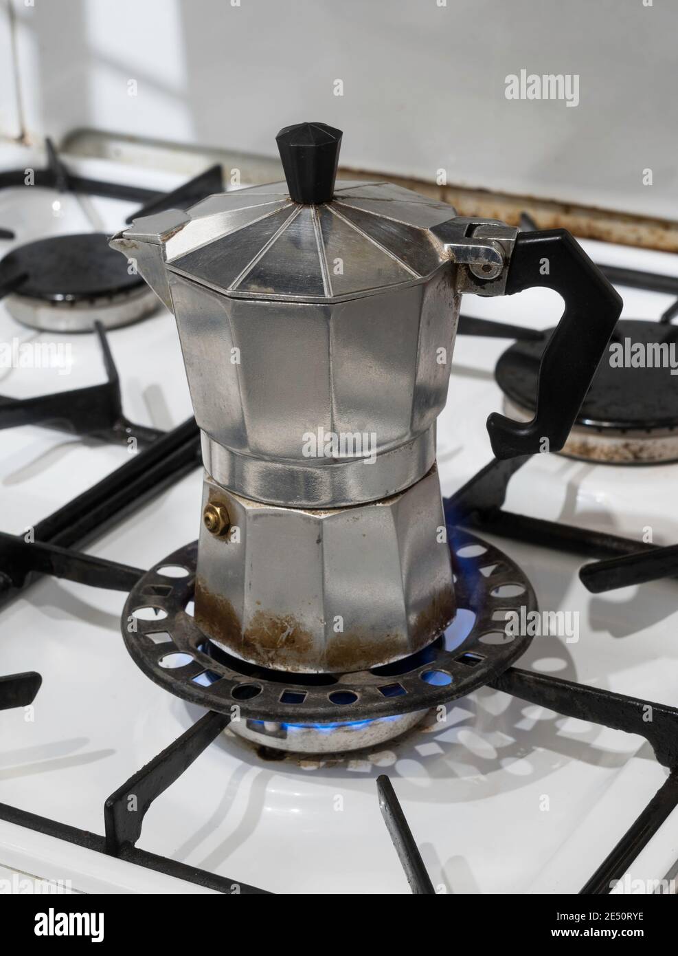 Una piccola caffettiera Moka su un piano cottura a gas utilizzando un trivet ad anello riduttore Foto Stock