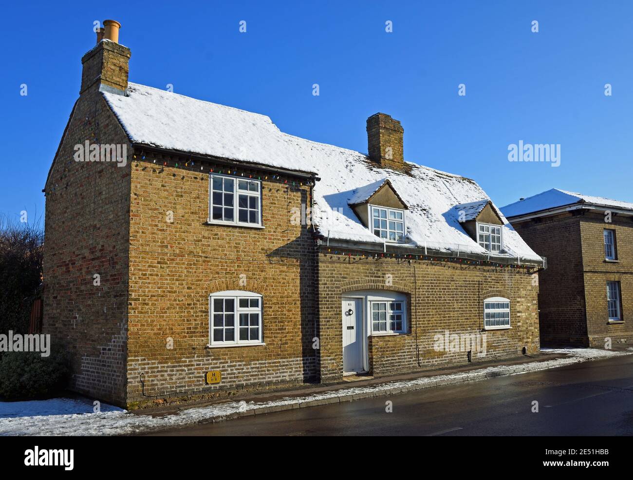 Old Cottage con neve sul tetto e cielo blu, Foto Stock