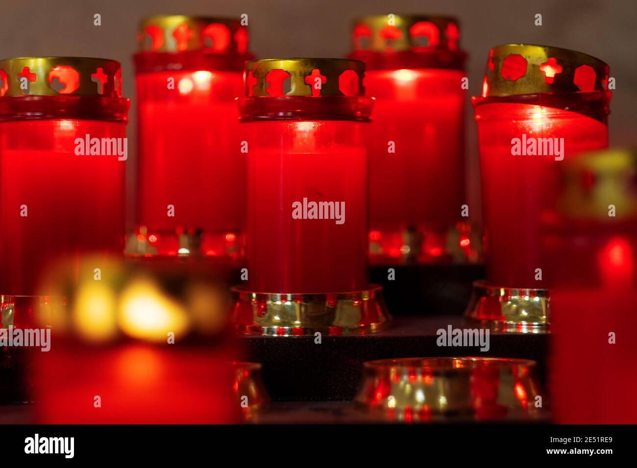 Una rastrelliera di candele rosse votive di preghiera in una chiesa italiana. Le fiamme a lume di candela in fila sono simbolo di religione silenziosa per la pace, la vita e l'anima. Foto Stock