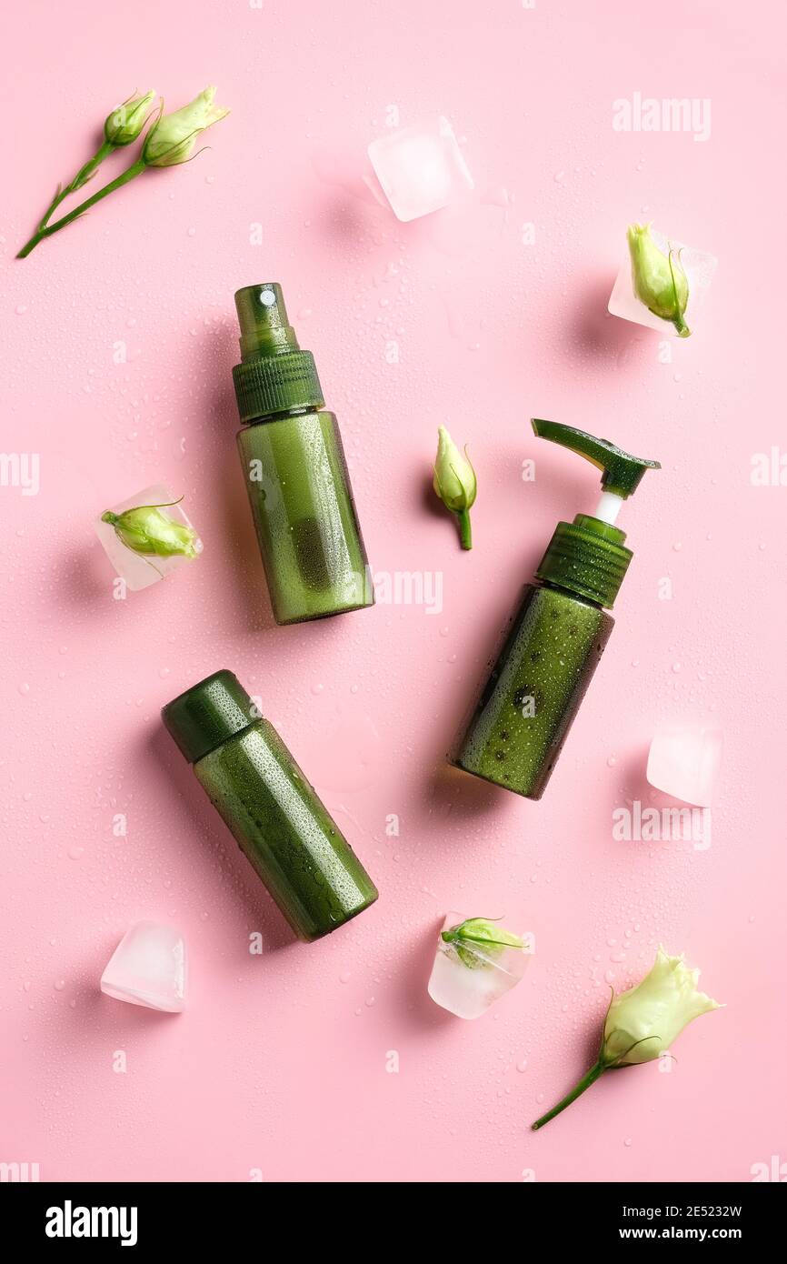 Contenitori cosmetici verdi, fiori, cubetti di ghiaccio su sfondo rosa. Concetto di prodotti di bellezza naturale. Foto Stock