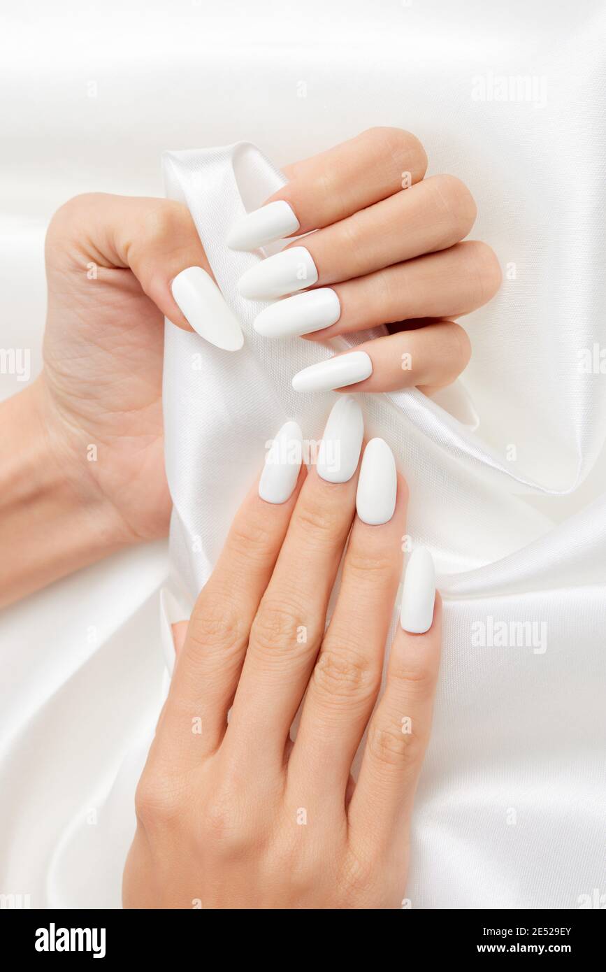 Scatto verticale delle mani di una donna con smalto bianco per unghie su un  tessuto di seta bianco Foto stock - Alamy