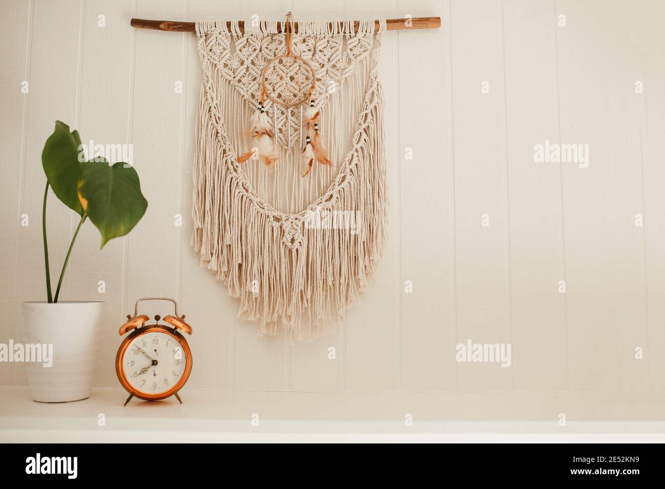 Camino in legno bianco con macrame e sogni catcher sulla parete, con piante casa e allarme rame vintage sulla mensola fuoco posto Foto Stock