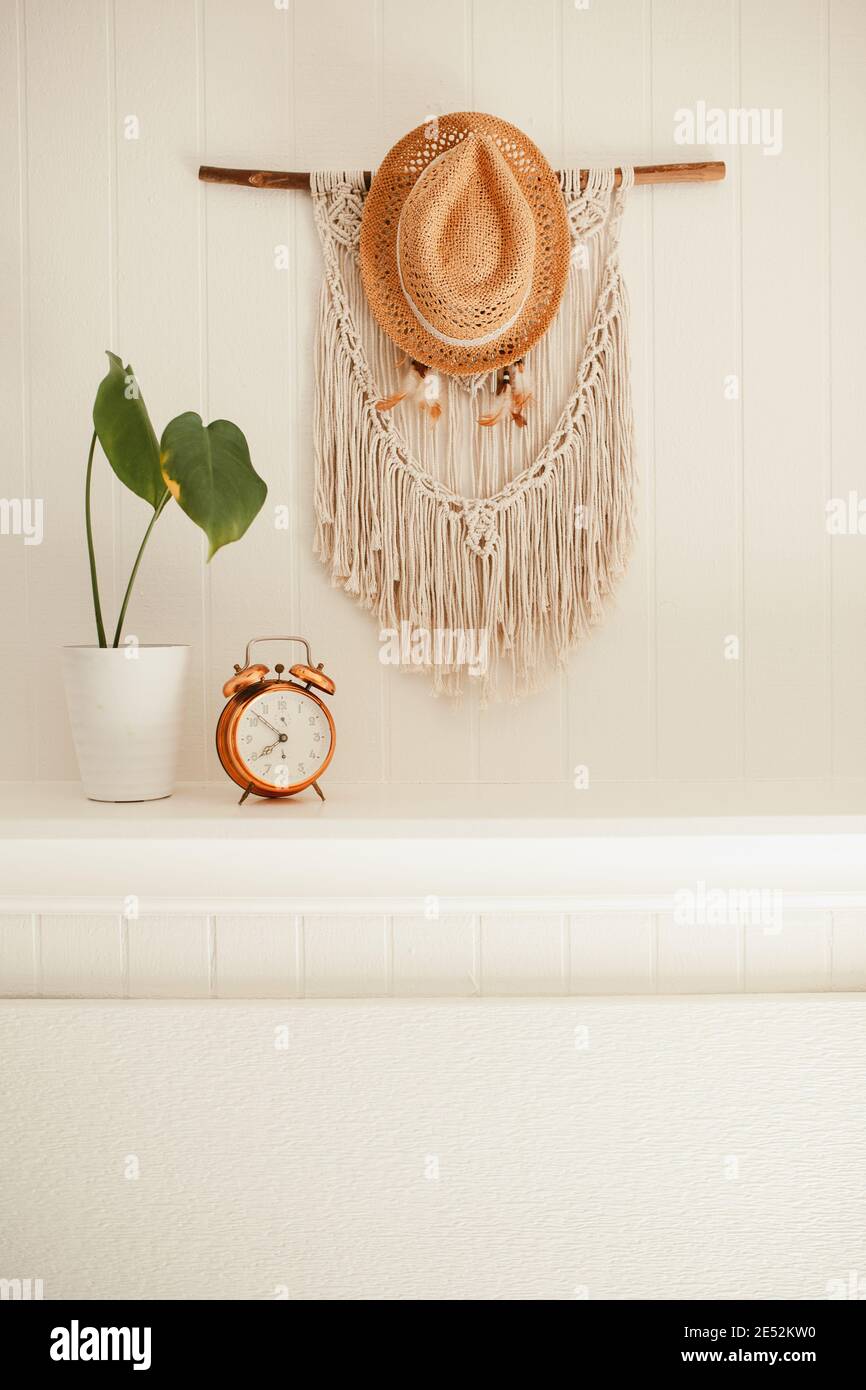 Camino in legno bianco con macrame e sogni catcher sulla parete, con piante casa e allarme rame vintage sulla mensola fuoco posto Foto Stock