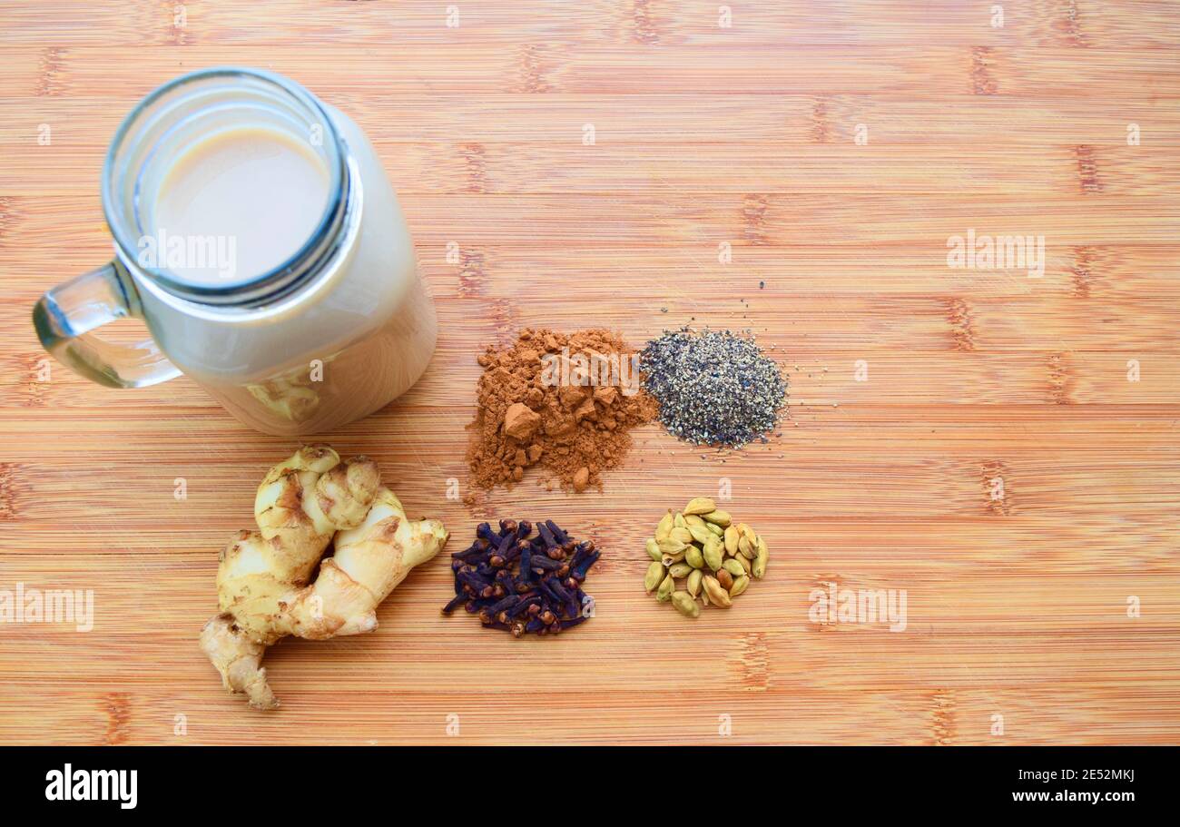 Bevanda calda fatta in casa Chai latte, con tutte le spezie utilizzate incluse, su un tagliere di legno. Foto Stock