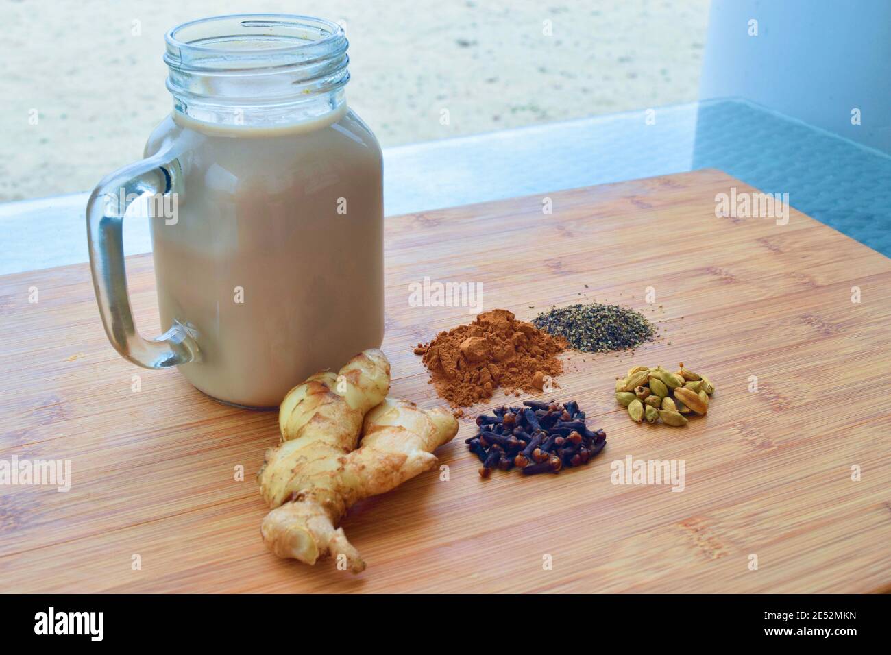 Bevanda calda fatta in casa Chai latte, con tutte le spezie utilizzate incluse, su un tagliere di legno. Foto Stock