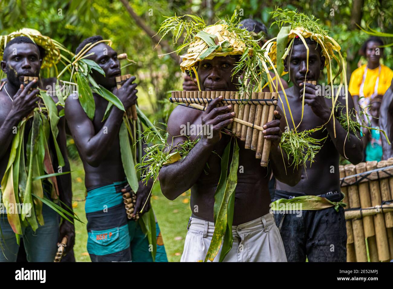 Giocatori di panflute con copricapi di paglia gialli stanno in semicerchio durante un Sing-Sing tradizionale sull'isola di Tautsina vicino a Bougainville, Papua Nuova Guinea, le barre di bambù di uno xilofono sono visibili a destra. Foto Stock