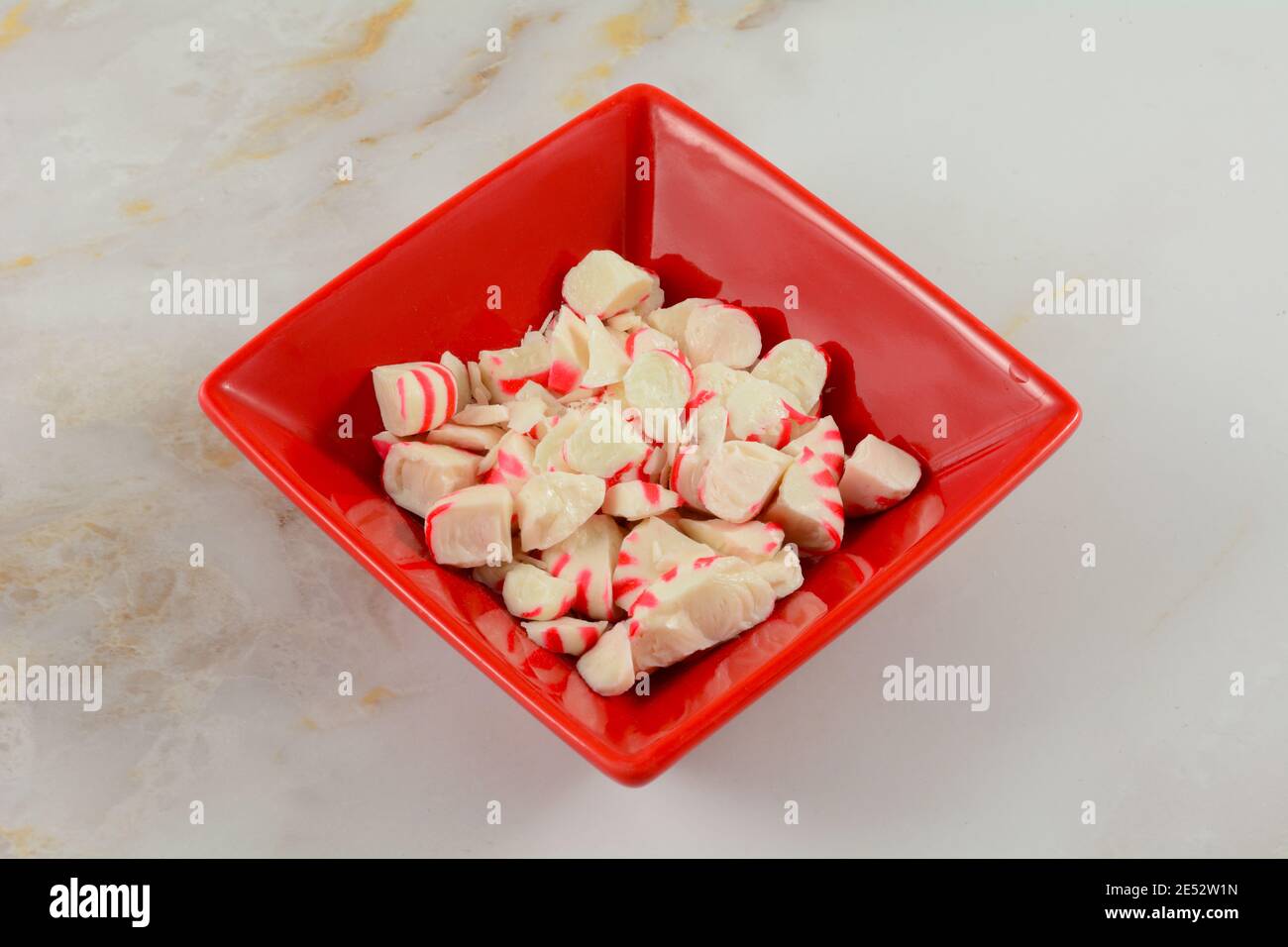 Pezzi di caramelle alla menta piperita schiacciati in una ciotola di ingredienti rossi sul tavolo Foto Stock