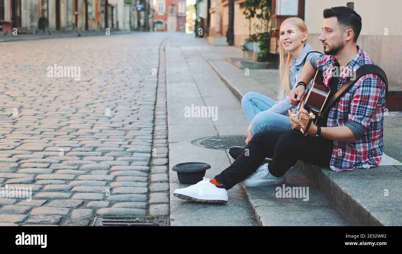 Un giovane paio di cantanti di strada nella parte vecchia della città,  seduti sul marciapiede. Uomo che suona la chitarra e donna che canta Foto  stock - Alamy