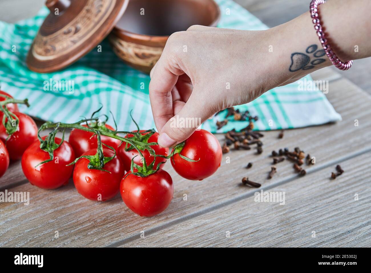 Mazzo di pomodori con rametto e donna che tiene un pomodoro su tavolo di legno Foto Stock