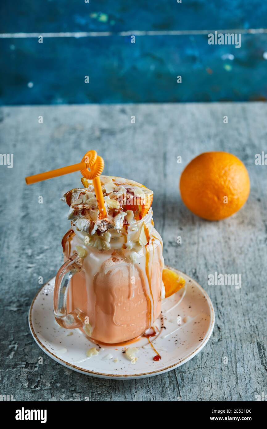 Frullato arancione con crema, paglia e fette di arancio sullo sfondo di marmo Foto Stock