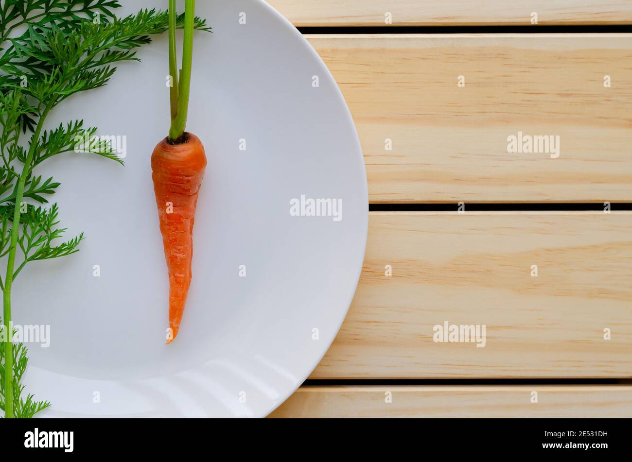 Carota fresca biologica per bambini con il suo albero su piastra bianca con fondo in legno. Foto Stock