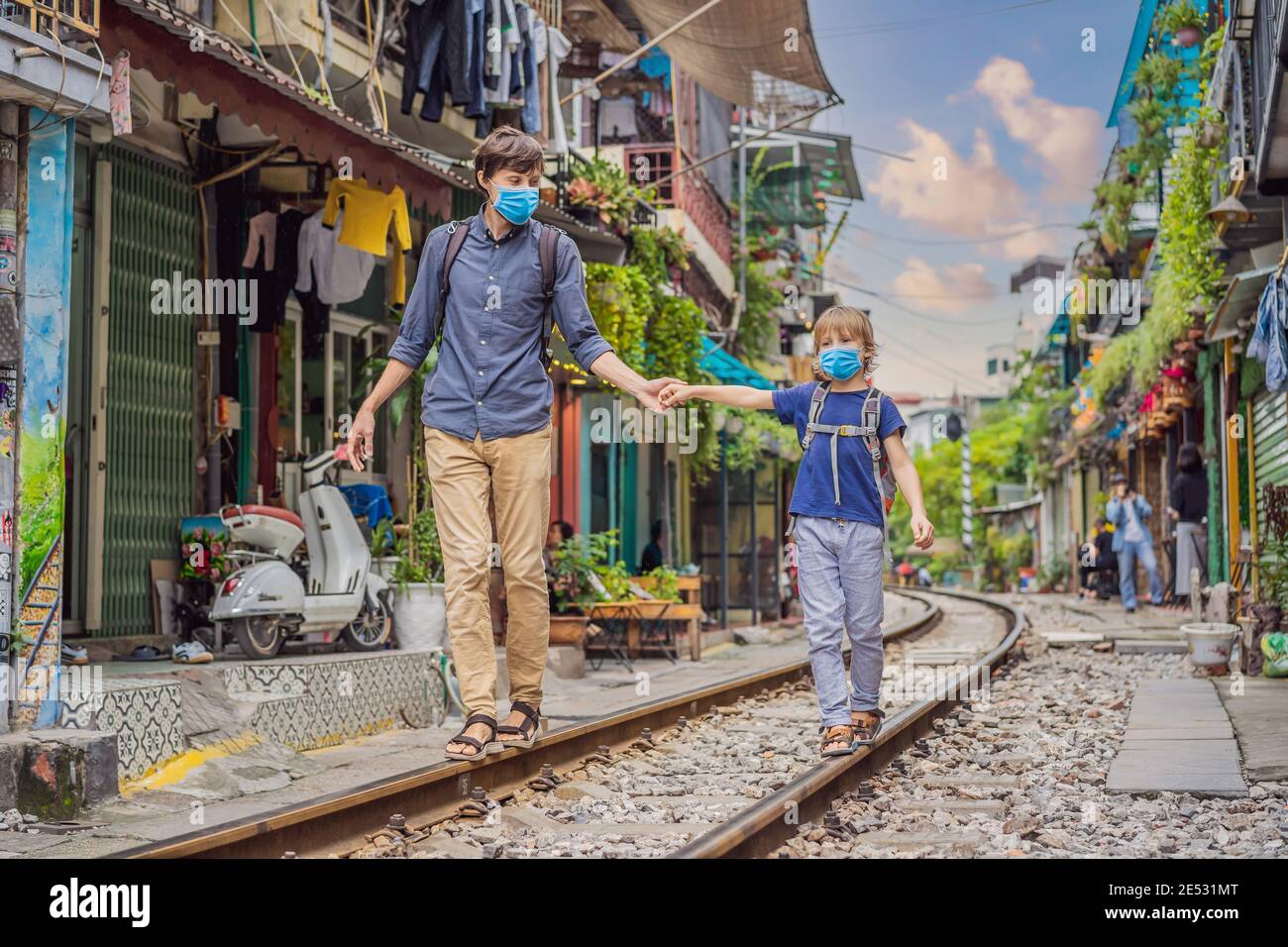 I viaggiatori del padre e del figlio che indossano una maschera medica durante COVID-19 passeggiata sul coronavirus lungo i sentieri ferroviari che attraversano l'area residenziale Nella città di Hanoi Foto Stock
