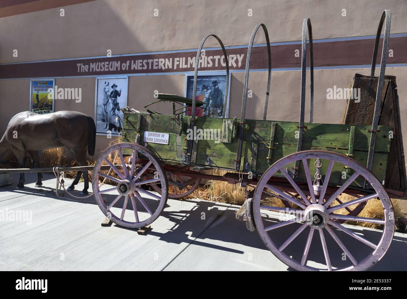 Replica vintage PioneerWestern Wagon Wheel di fronte al Museum of Western Film History di Lone Pine, California, con vecchi poster cinematografici sull'esterno della parete Foto Stock