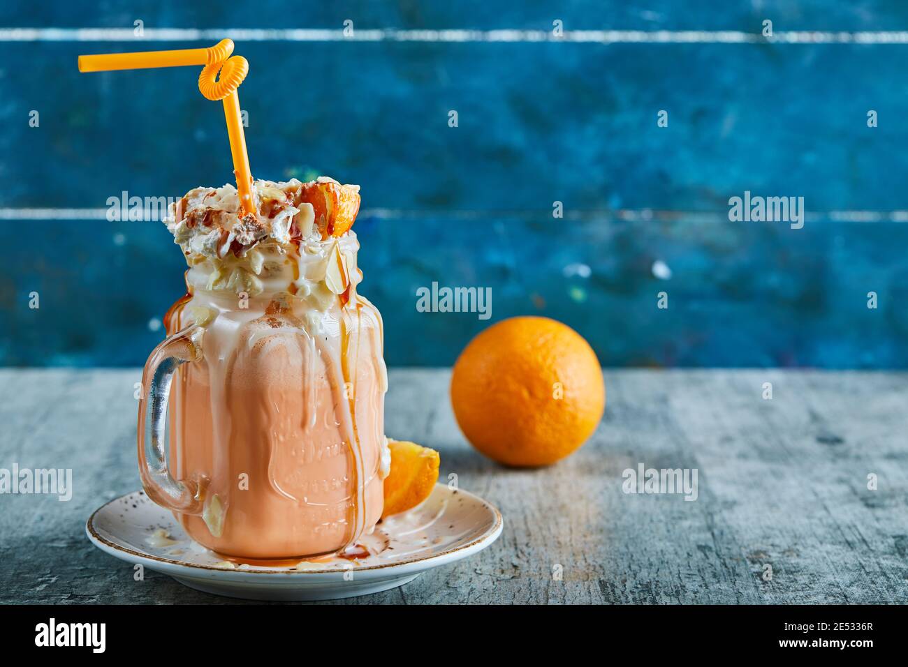 Frullato arancione con crema, paglia e fette di arancio sullo sfondo di marmo Foto Stock