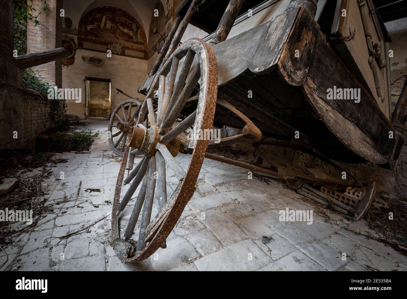 Primo piano di un'antica carrozza trainata da cavalli, sdraiata in un antico chiostro italiano abbandonato Foto Stock