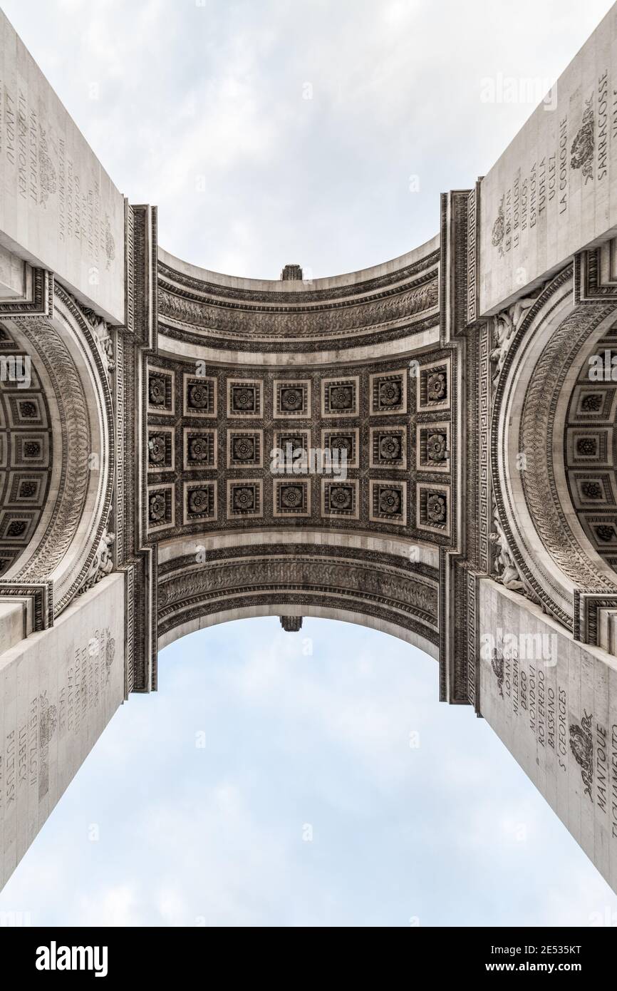 Scatto simmetrico dal basso dell'Arco di Trionfo visto dal basso, contro un cielo blu con nuvole soffici Foto Stock