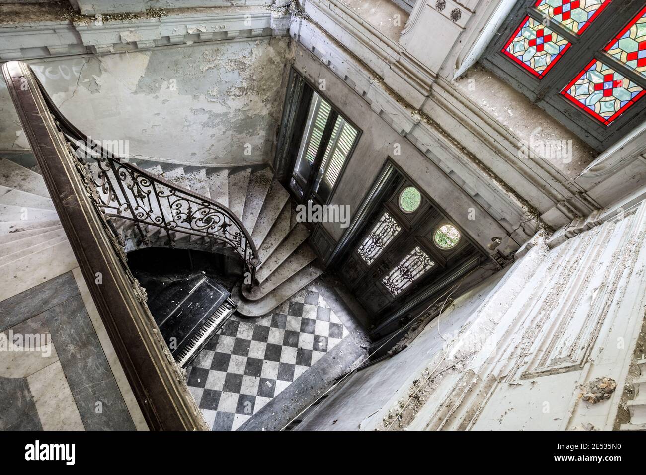 Ampia vista angolare della scalinata in marmo di un vecchio e abbandonata casetta francese con finestre in vetro colorato e un pianoforte a terra Foto Stock