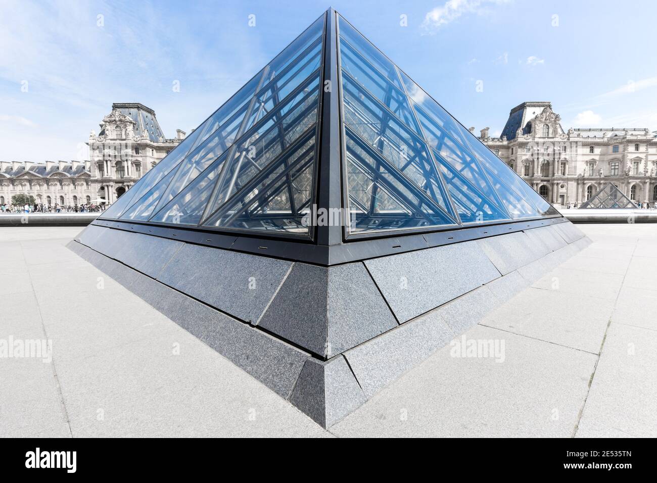 Vista grandangolare simmetrica della Piramide del Louvre, sotto un cielo estivo blu con nuvole sparse Foto Stock
