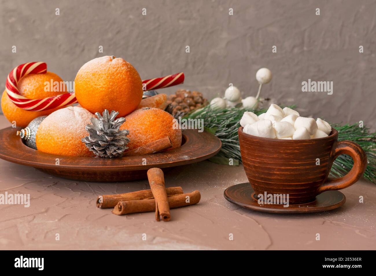 Composizione di Natale. Coppa di argilla con marshmallows, tangerini, caramelle e coni su tavola di cemento. Messa a fuoco selettiva, sfondo sfocato. Foto Stock