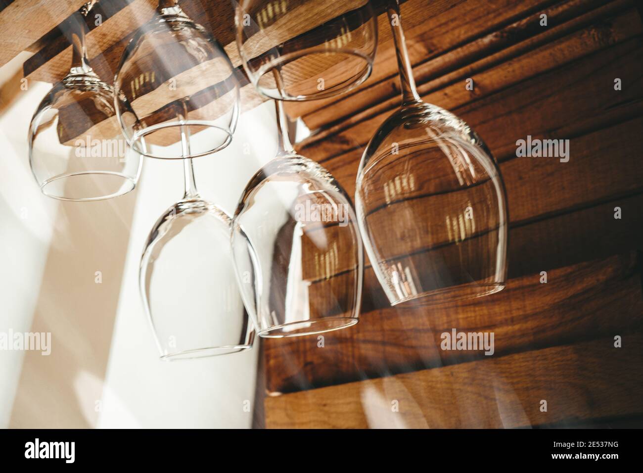 Bicchieri da vino frizzanti con pulizia appesi al bancone del bar in condizioni di luce solare intensa da vicino Foto Stock