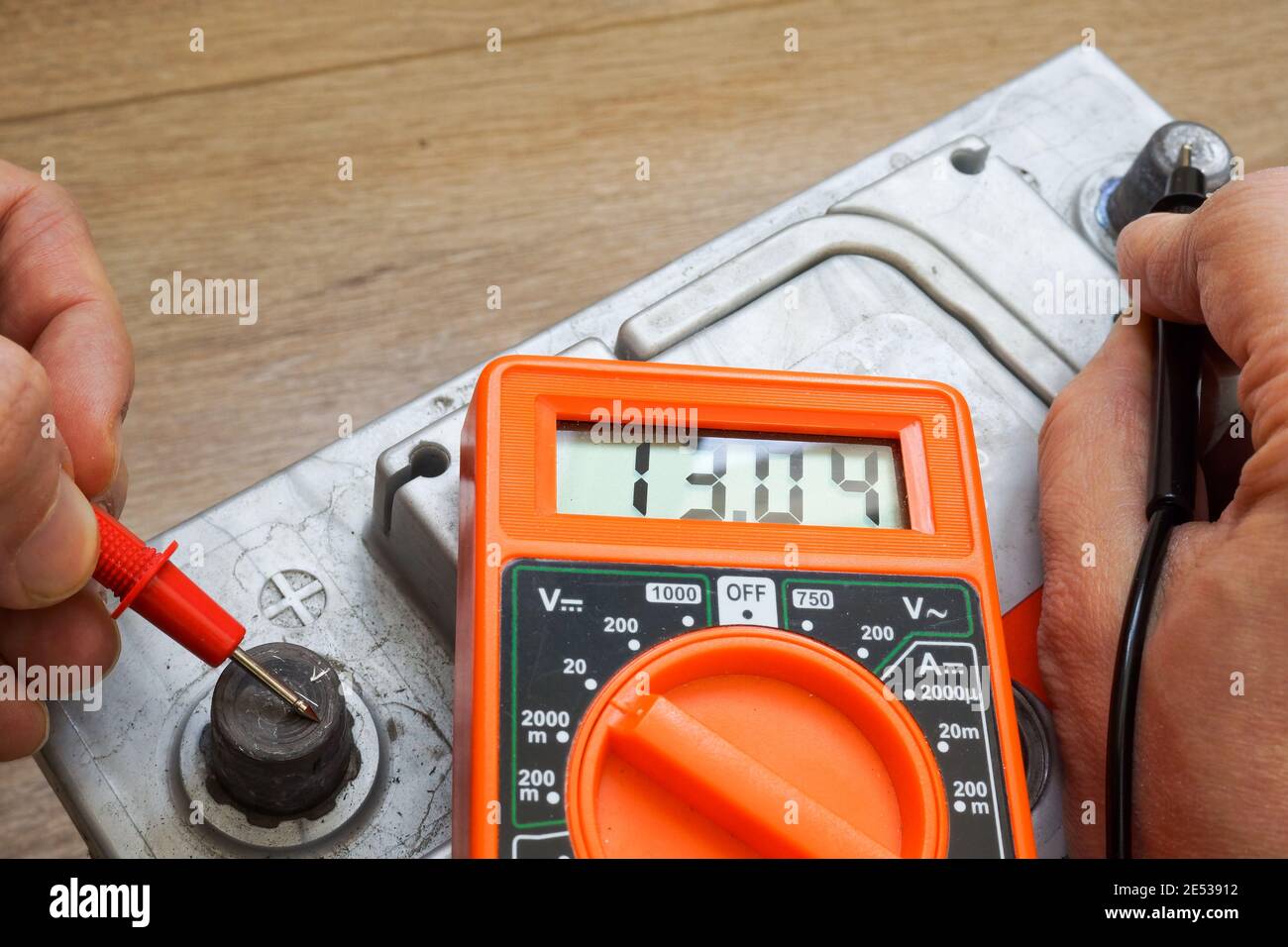 Mani con un voltmetro controllare il livello di carica della batteria dell'auto. Foto Stock