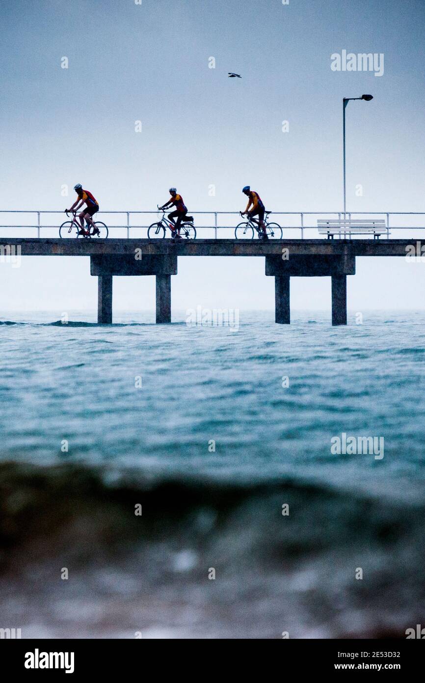 Ciclisti in giro sotto la pioggia sul molo a Cowes, Phillip Island. Foto Stock