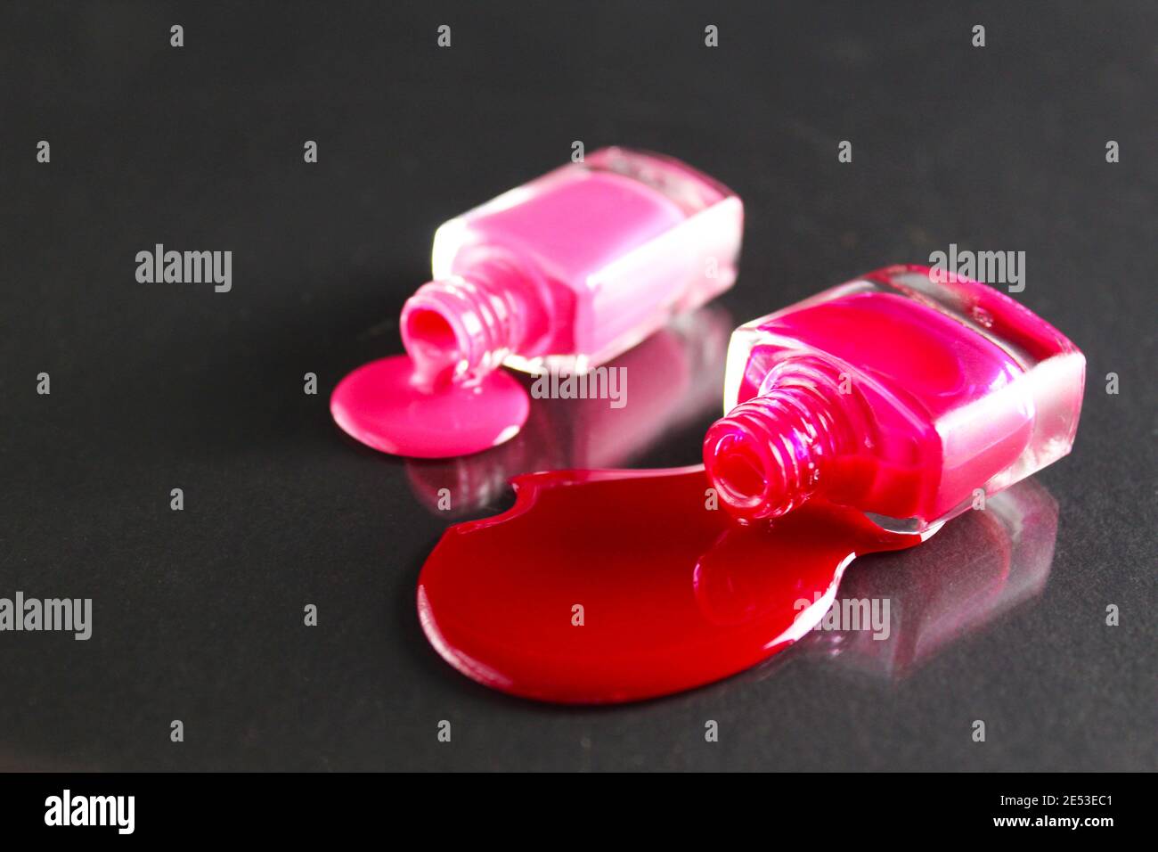 Fondo di bellezza due bottiglie di smalto per unghie bottiglie rosso o rosa bordeaux versamento sul tavolo su uno sfondo nero con un copyspace . Foto Stock