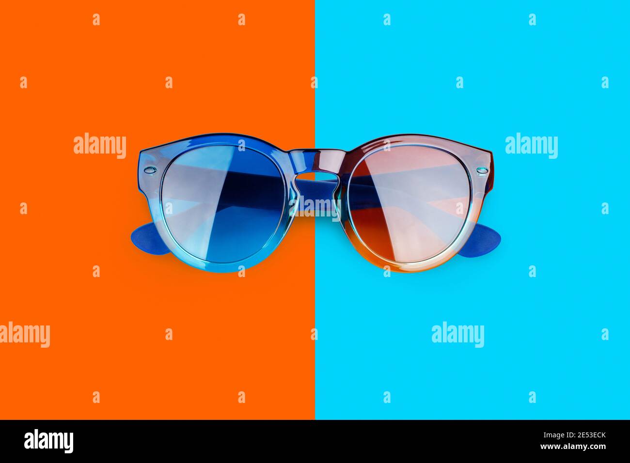 Occhiali da sole sfondo blu e rosso arancio primo piano vista dall'alto, ombrelloni alla moda su sfondo colorato, occhiali alla moda, vacanze estive in spiaggia Foto Stock