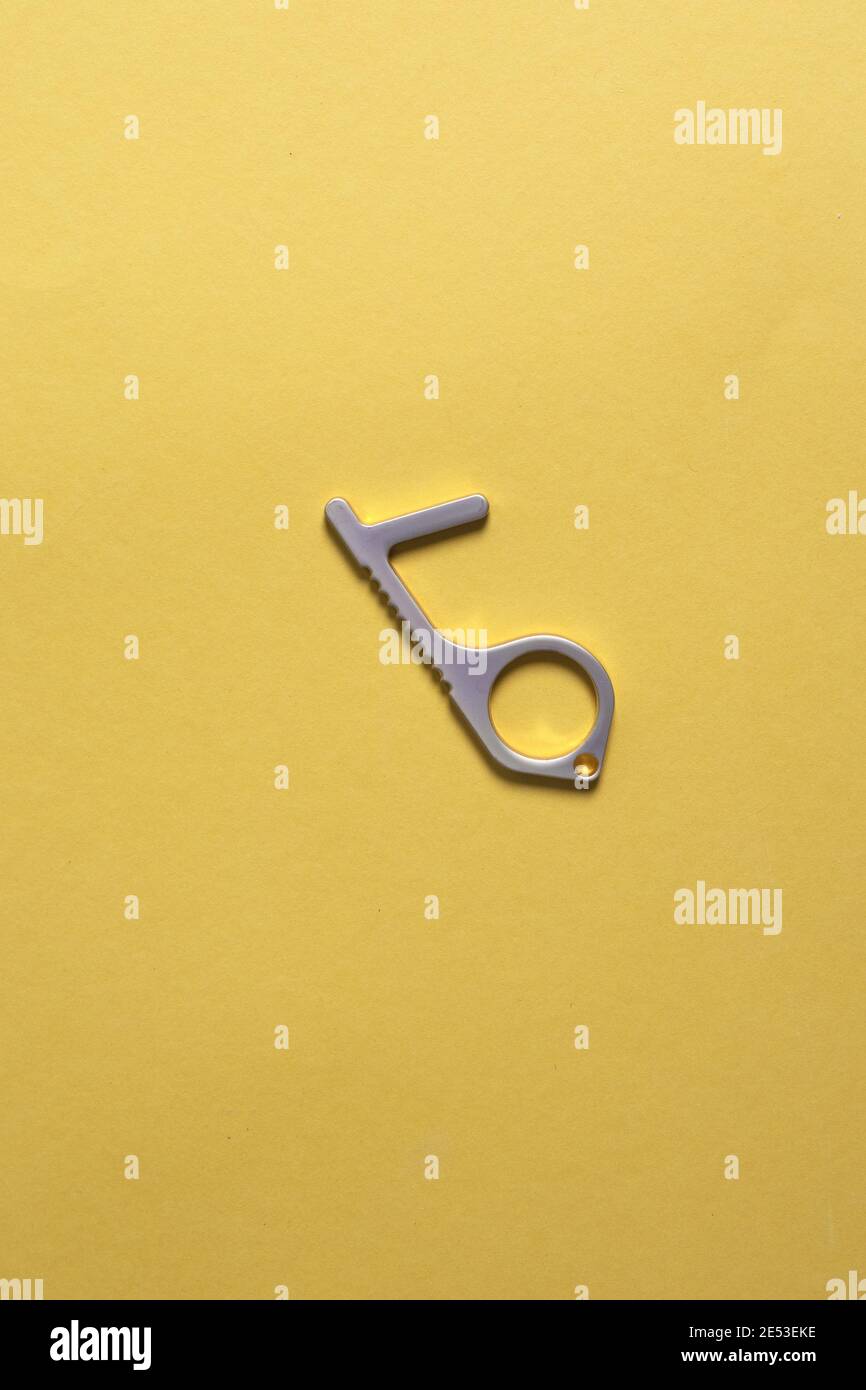 Impugnatura in ottone per aprire le porte e premere i pulsanti senza toccarle. Protezione senza contatto antibatterico senza contatto su sfondo giallo Foto Stock