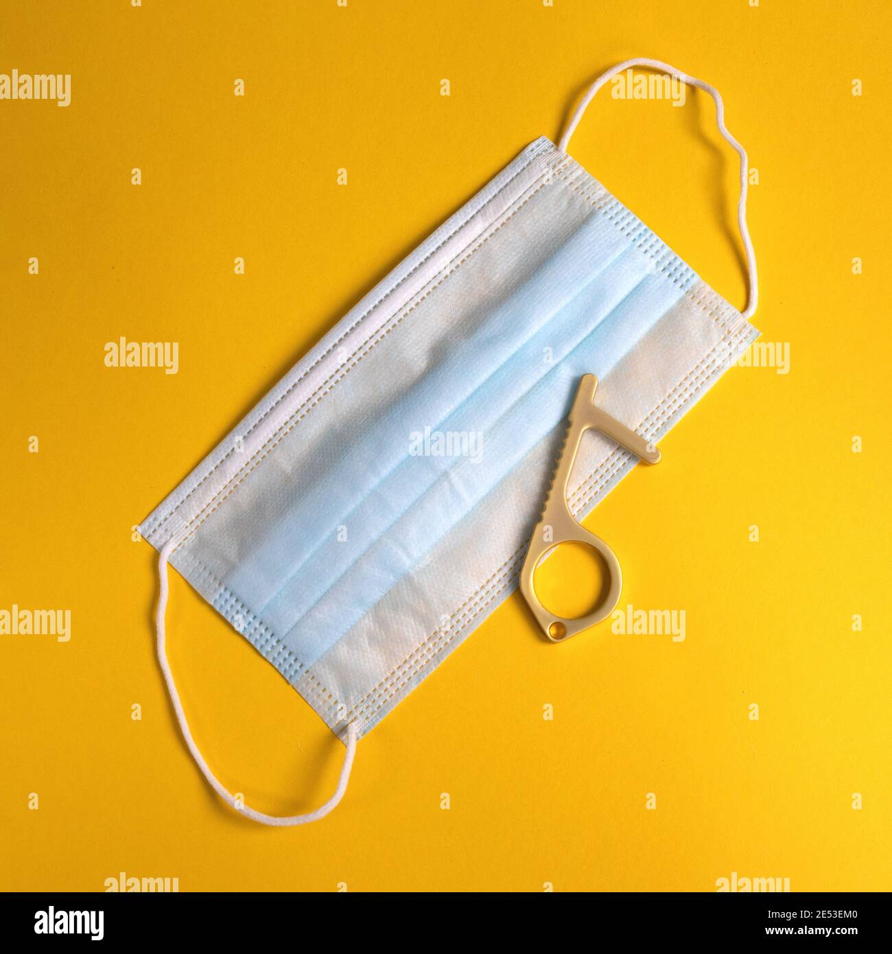 Maschera chirurgica e pulsante ascensore senza contatto, senza contatto maniglia sportello di apertura su sfondo giallo. Prevenire l'infezione da virus Foto Stock