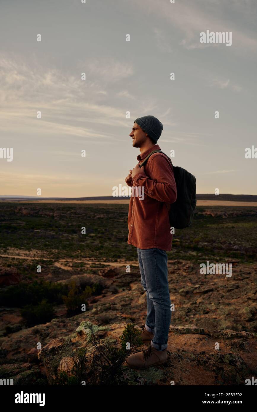 Escursionista di successo con borsa e berretto in piedi sulla scogliera di montagna guardando l'alba del mattino Foto Stock