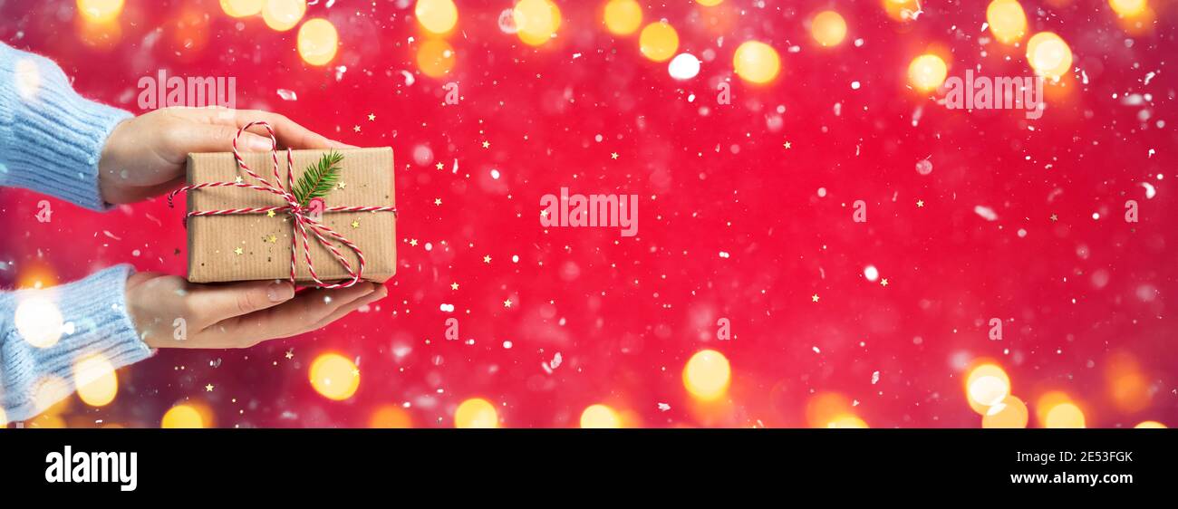 Le mani della donna danno un regalo rustico con nevica e luci Foto Stock