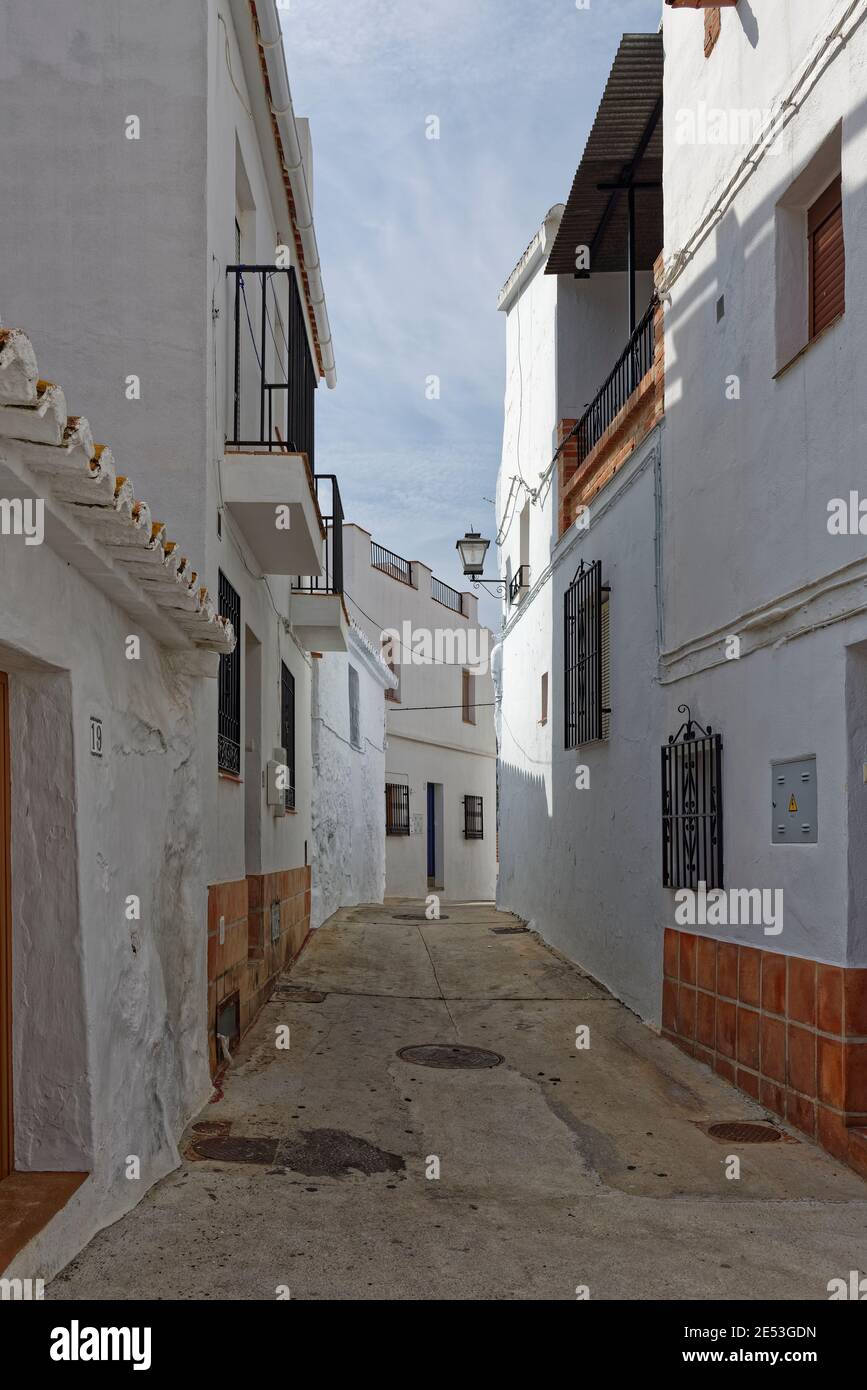 Una stretta strada di case tradizionali spagnole terrazzate, ombreggiate dal sole di mezzogiorno nel villaggio montano di Sayalonga in Andalusia. Foto Stock