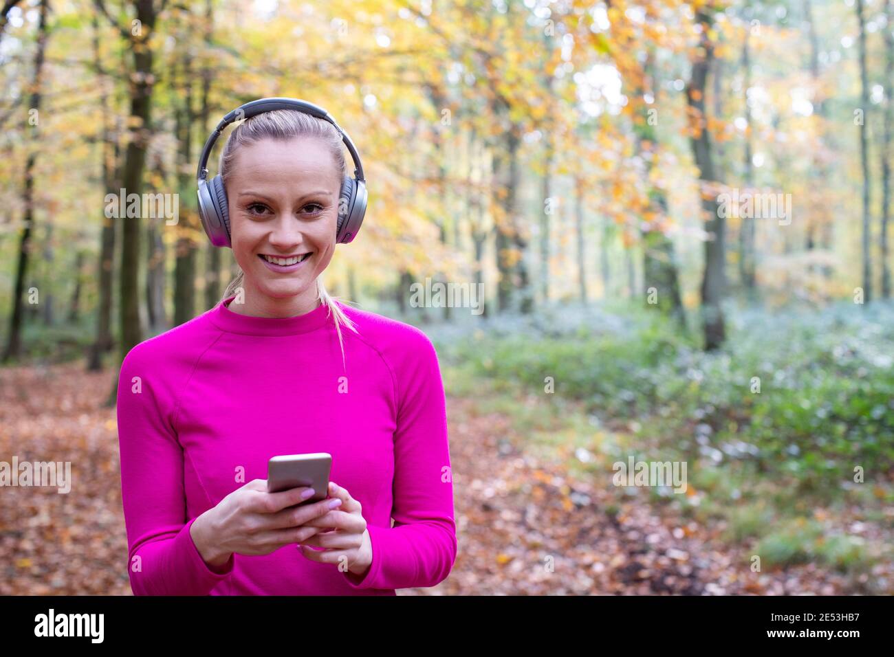 Ritratto di Donna scelta della musica da ascoltare sul cellulare Telefono prima di esercitarsi in Autunno Woodland Foto Stock