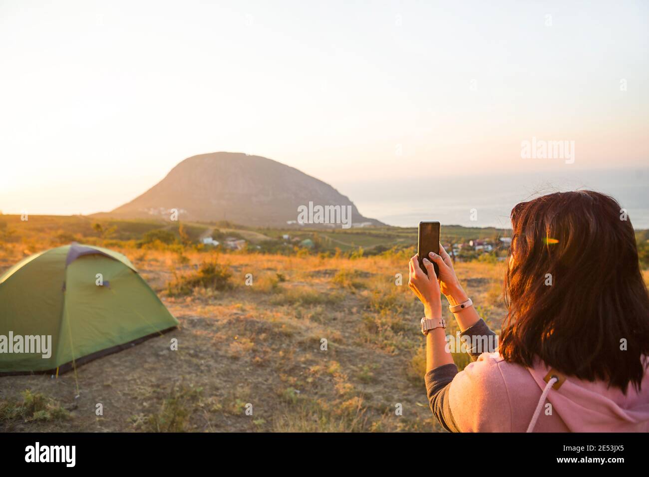 Donna scatta foto dell'alba in montagna sul suo telefono. Selfie nel sole nascente. Vista panoramica sul mare e Ayu-Dag. Campeggio, attività all'aperto, Foto Stock