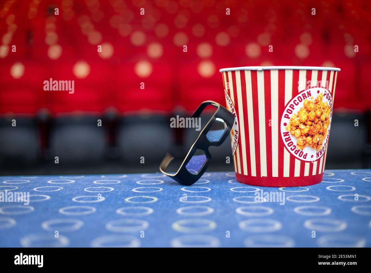 Un grande secchio di popcorn e occhiali 3D sul sfondo di sedie da cinema Foto Stock