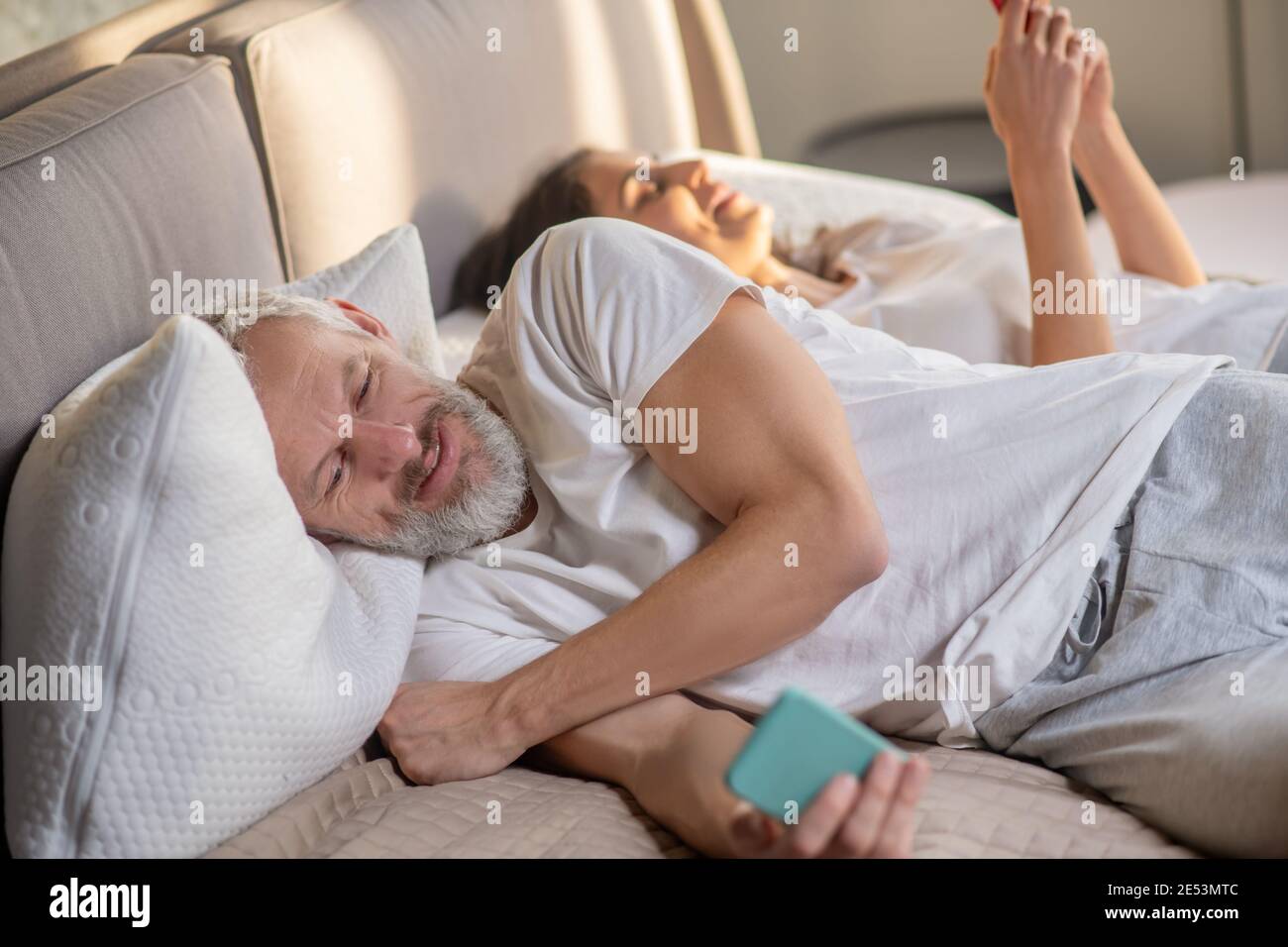 Uomo e donna con smartphone a letto Foto Stock