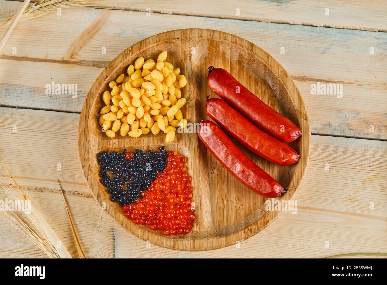 Salsicce, semi di mais bolliti e caviale su un piatto di legno Foto Stock