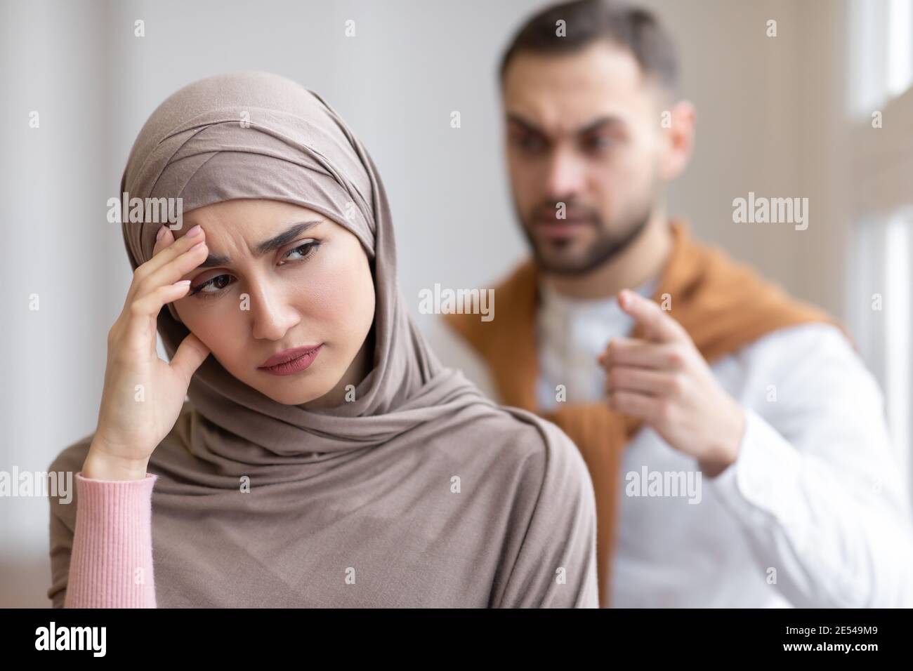 Marito musulmano aggressivo gridando alla moglie depressa in piedi a casa Foto Stock